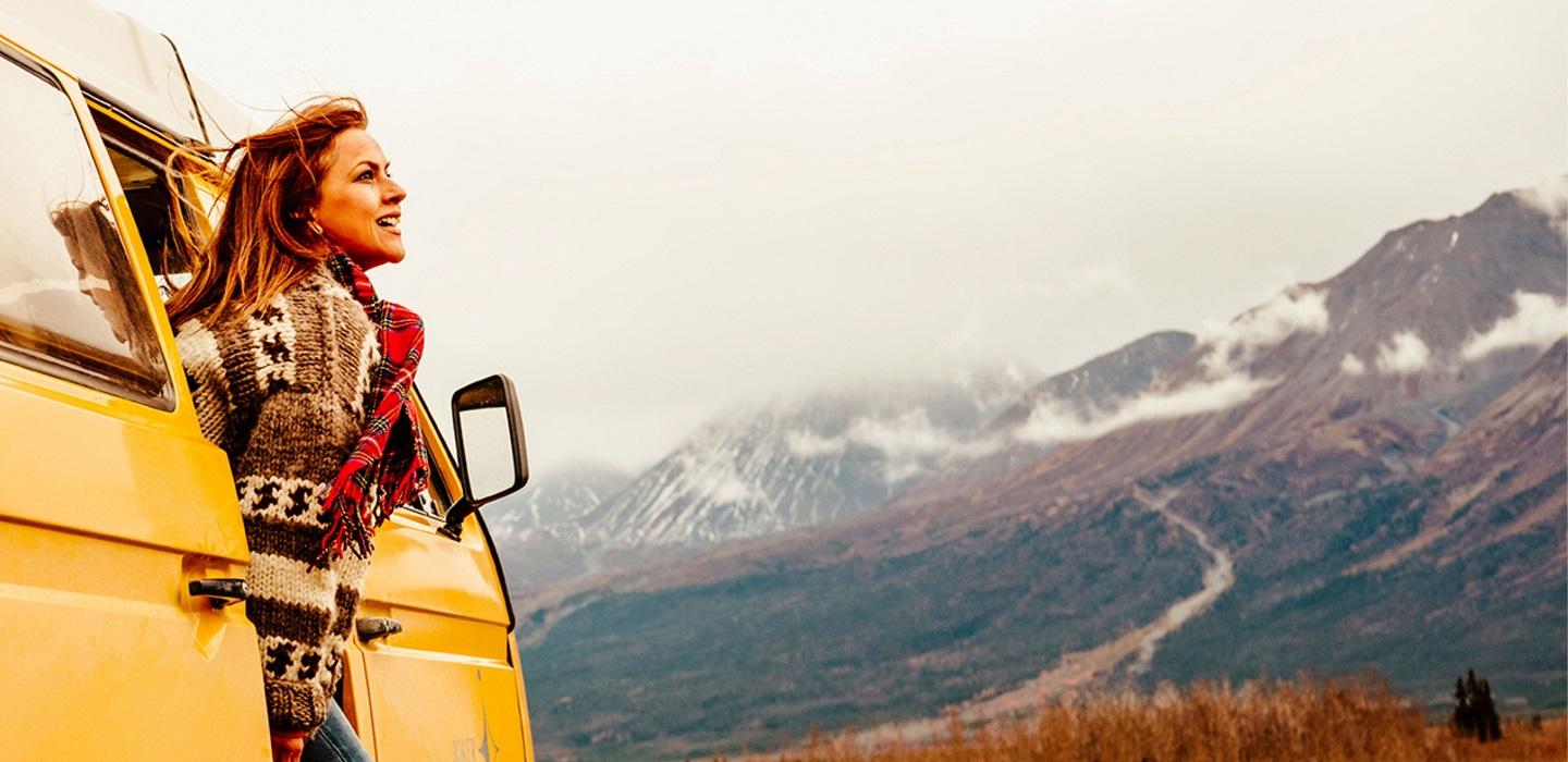 A woman looks out the door of her RV in the mountains