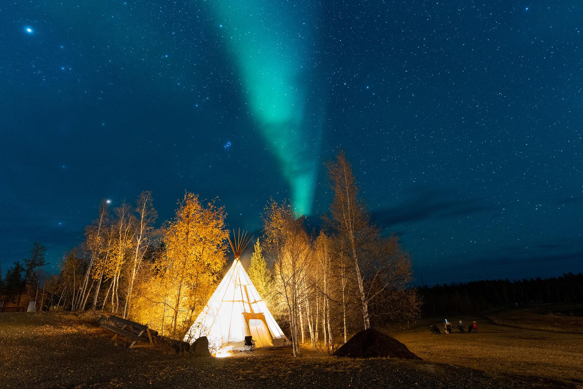 A tent in a forest, under the Northern Lights