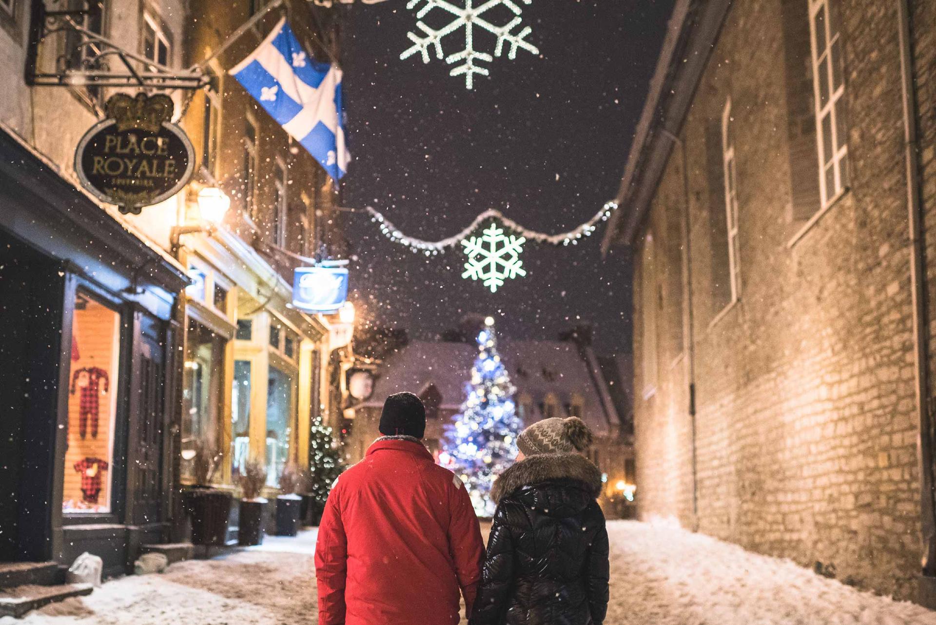 Two people walking down a snow-covered street in Vieux Quebec at night