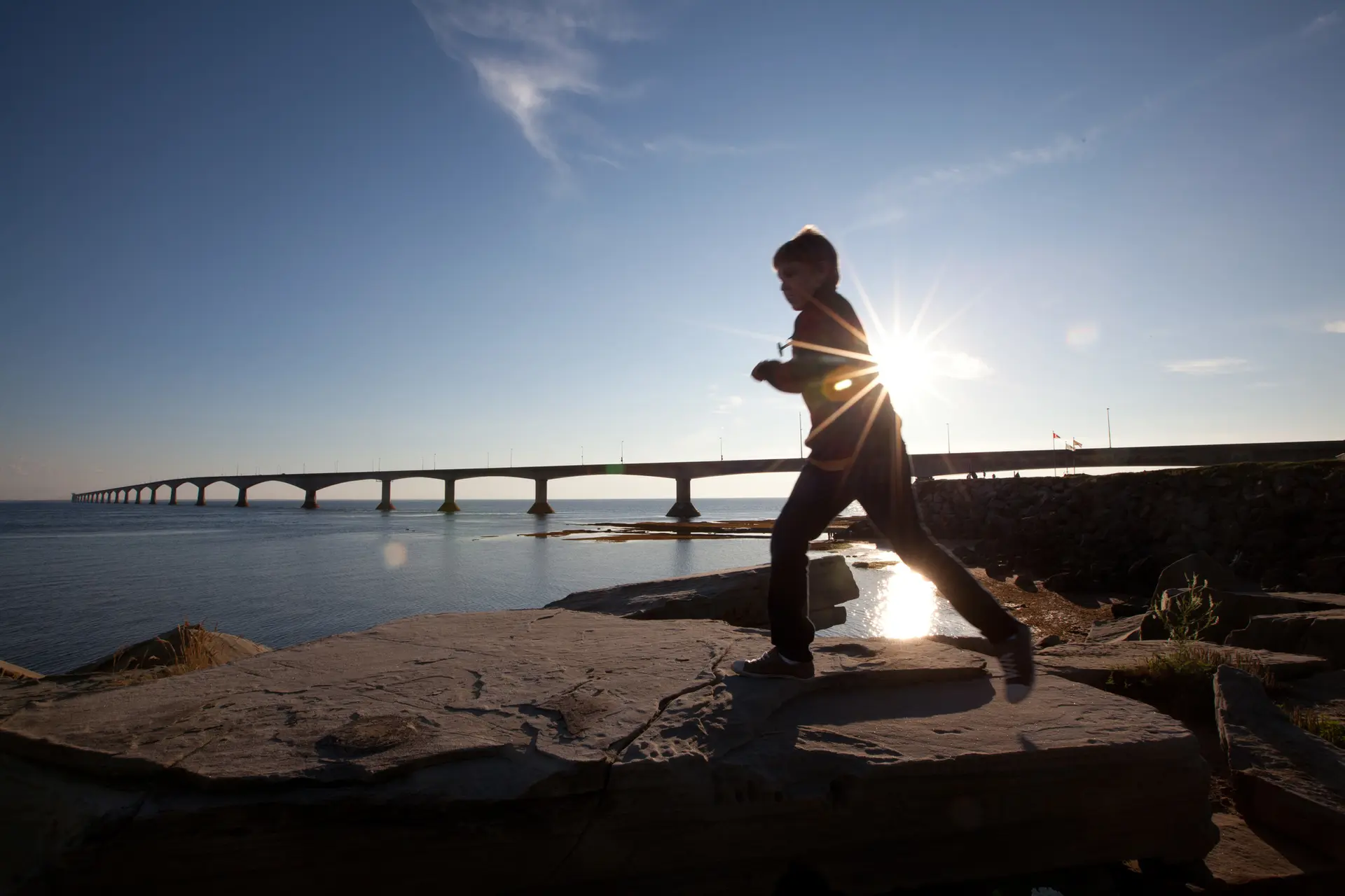 A young kid runs on the rocks under the Confederation Bridge in Prince Edward Island