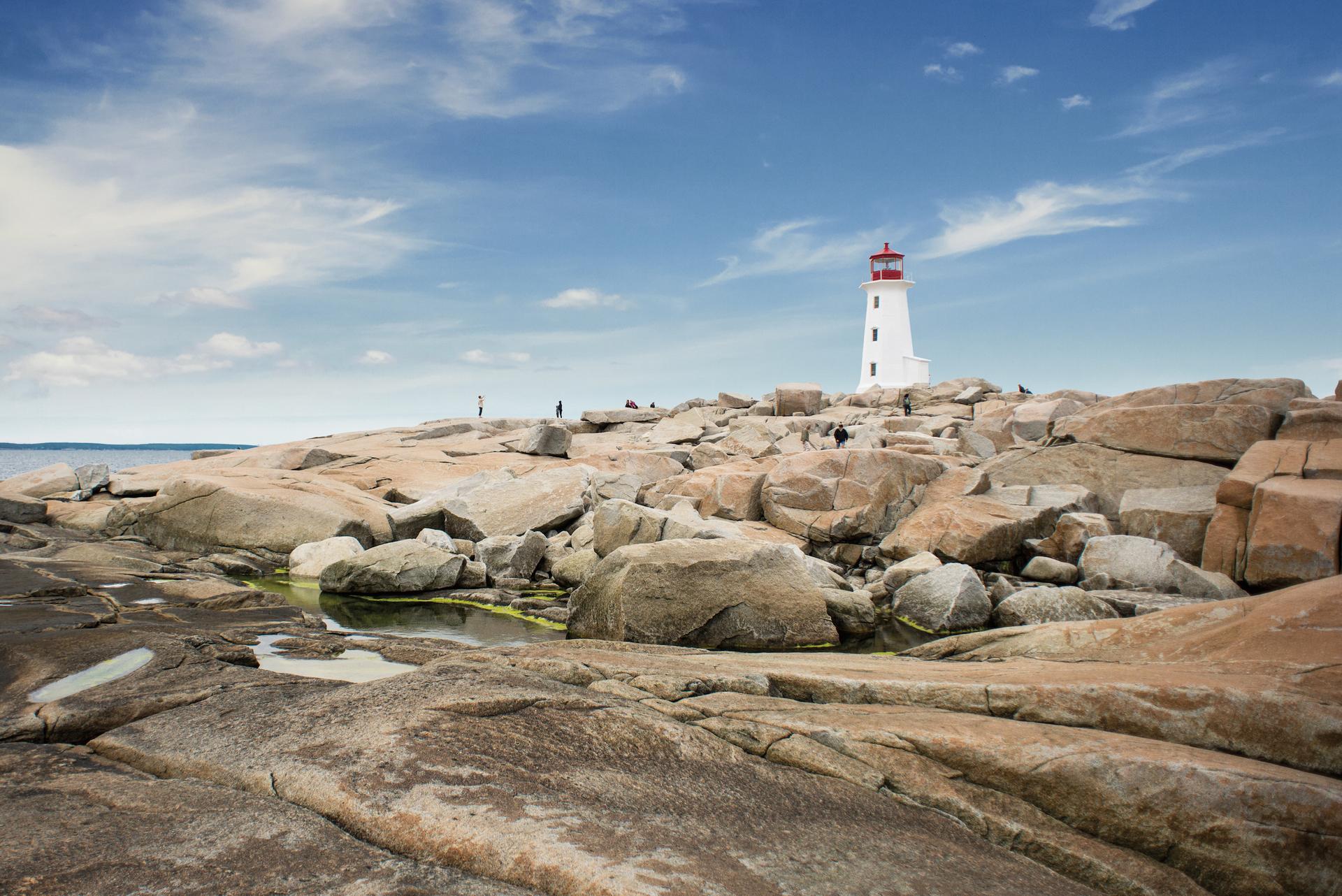 Visitors exploring the wave-worn granite rocks surrounding Peggy's Cove Lighthouse on Nova Scotia's Atlantic coast, the destination of VIA Rail's The Ocean train route from Montréal to Halifax