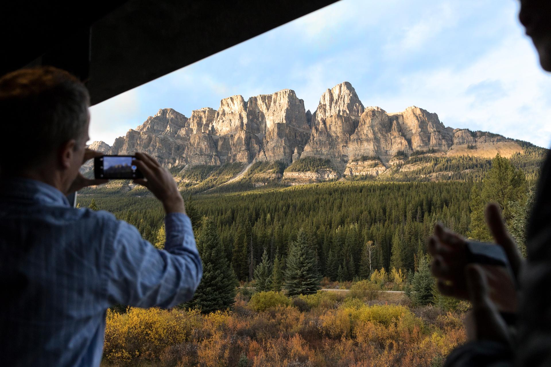 person taking a photo of mountain range from train seat