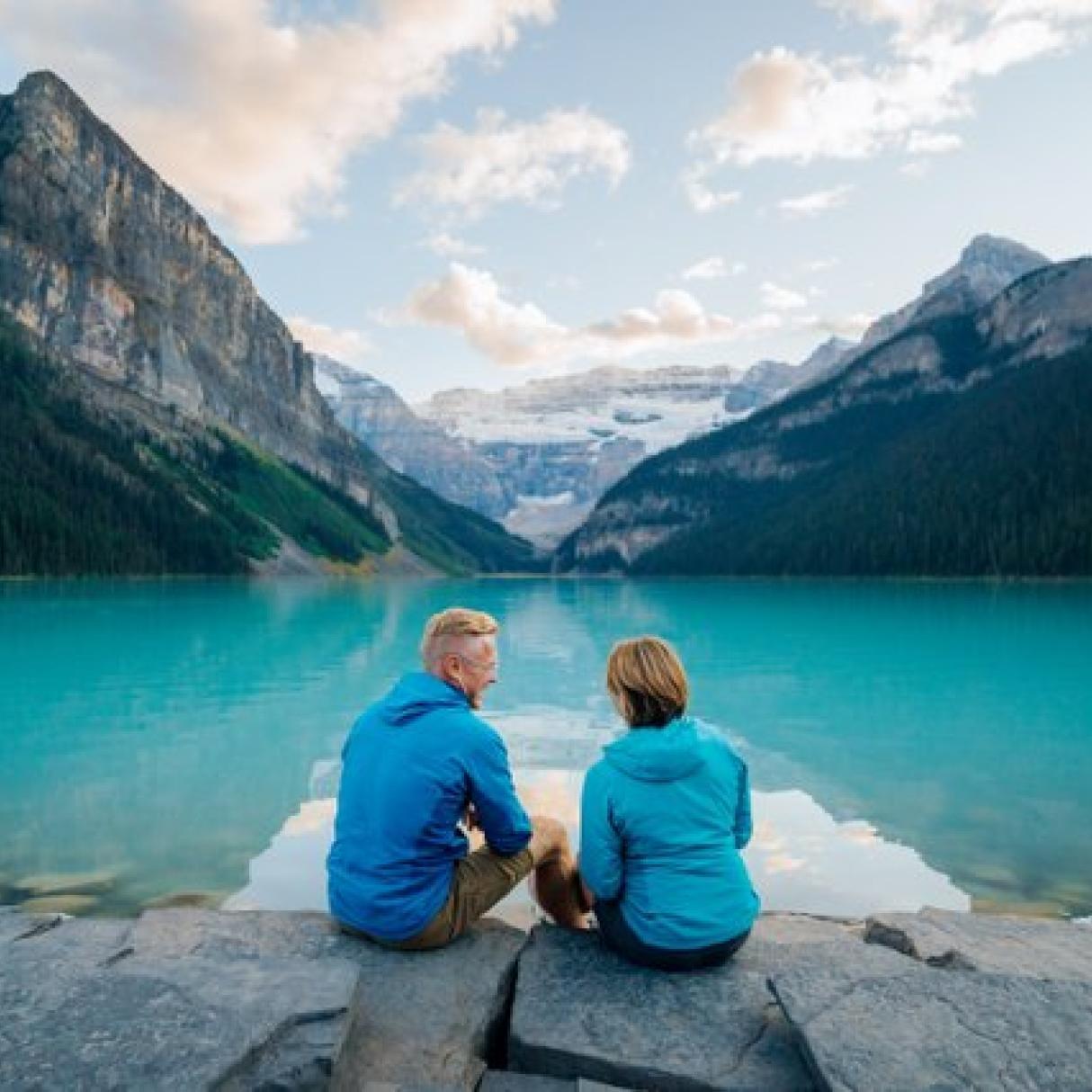 A couple sits by a lake in the mountains