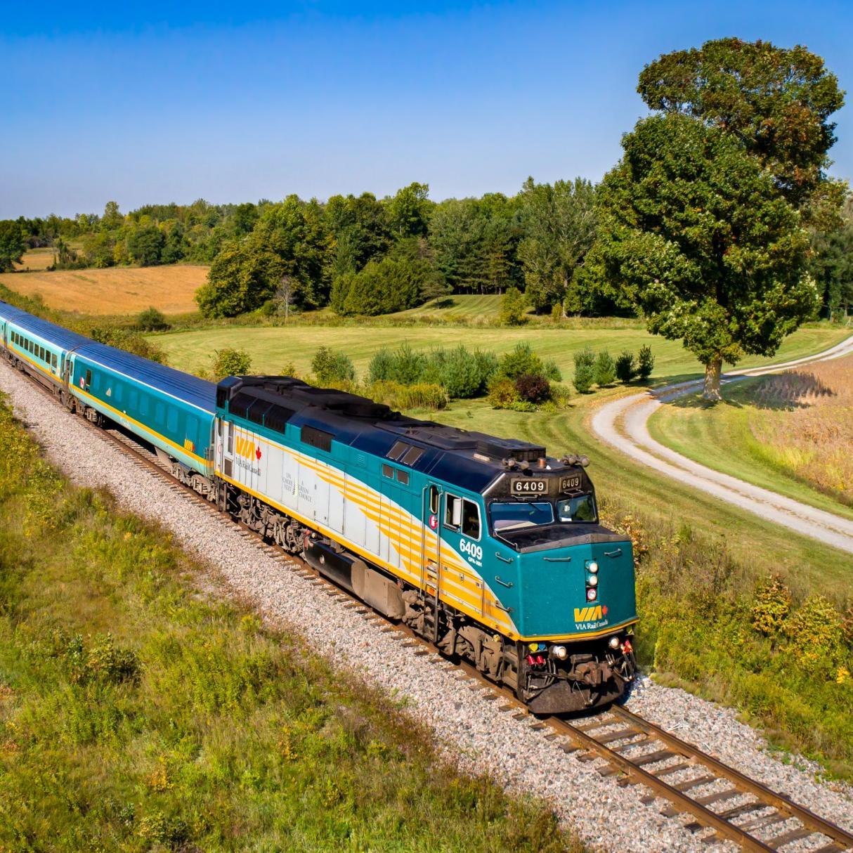 A Via Rail train travels through a green landscape