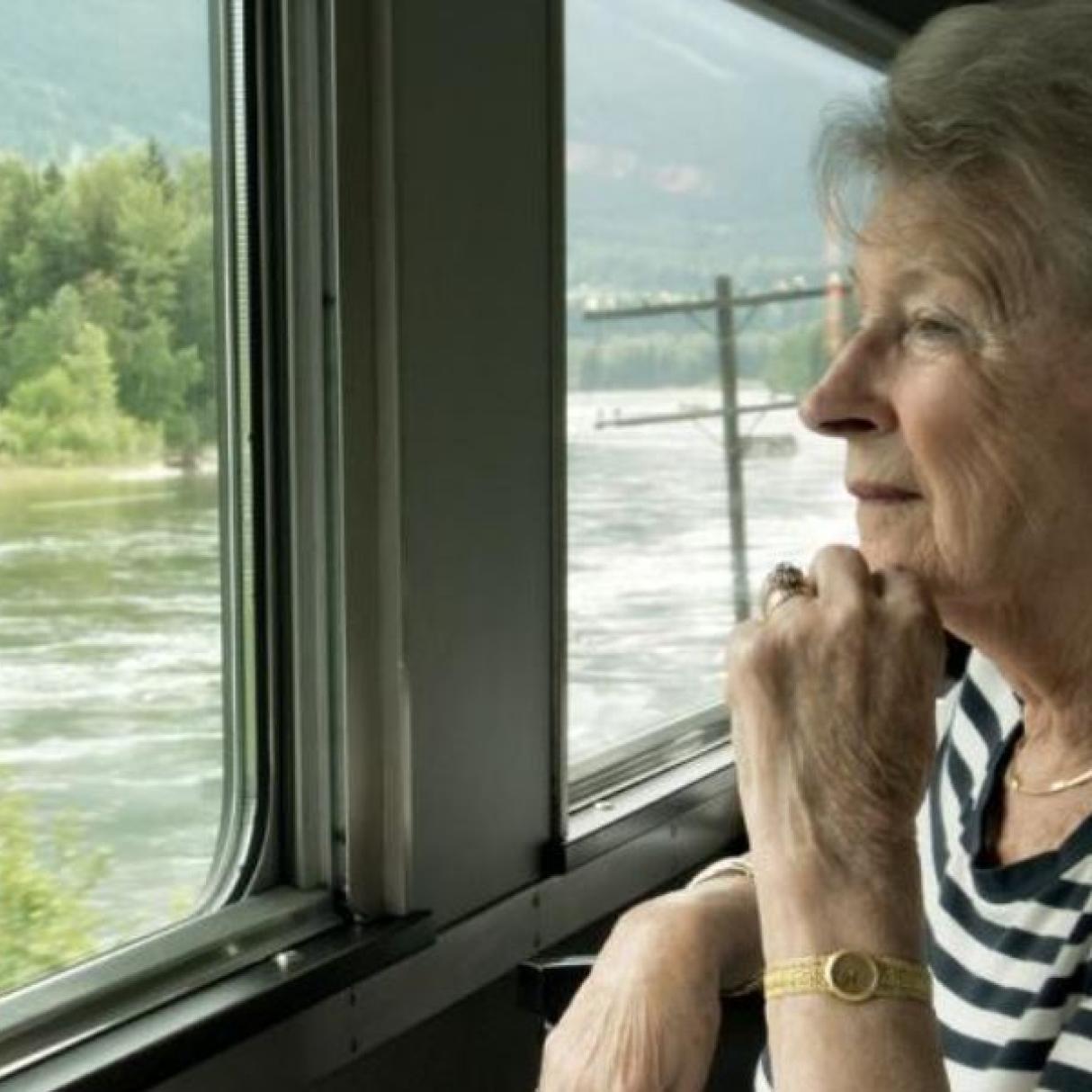 A woman looks out a train window at river and forest